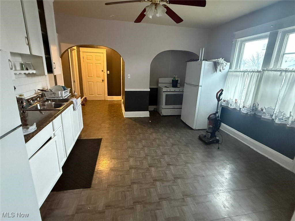 869 Whitcomb Road Cleveland, OH 44110 - Photo 5 of 8 Kitchen featuring white appliances, arched walkways, a ceiling fan, and white cabinets