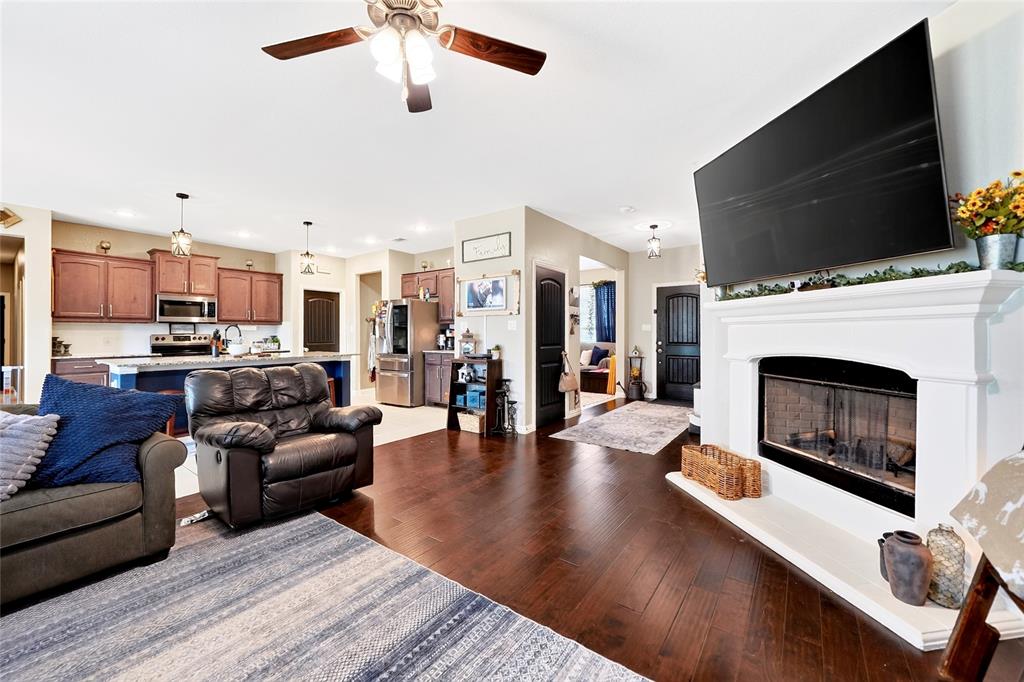 113 Ridgetop Trail Rhome, TX 76078 - Photo 5 of 32 Open-concept living area featuring rich wood-finish flooring, a white mantel fireplace, and a ceiling fan with integrated lighting