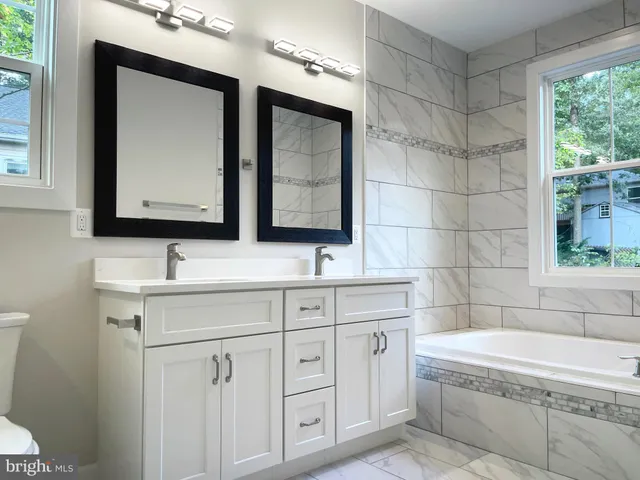 a bathroom with a double vanity sink a large mirror and bathtub