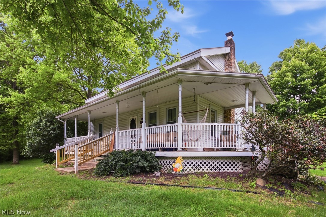 Property exterior featuring a full-width covered porch with white railings, a brick chimney, and siding facade