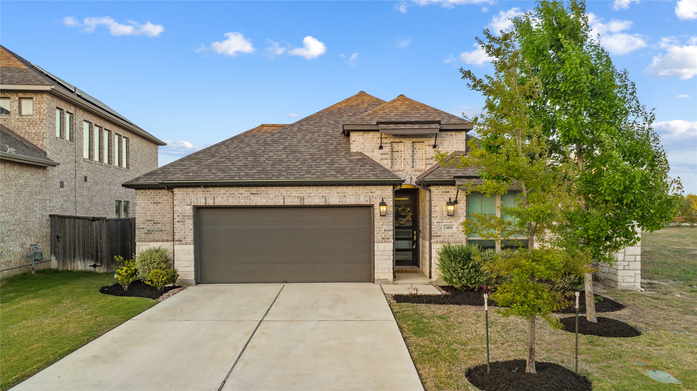 French country inspired facade featuring brick siding, a garage, a front yard, concrete driveway, and a shingled roof