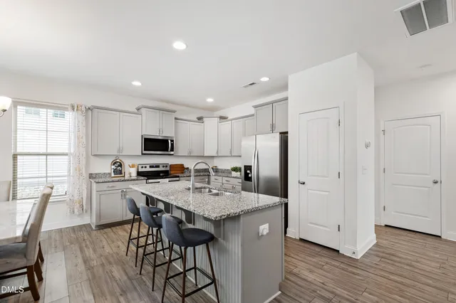 a kitchen with stainless steel appliances granite countertop a stove top oven a sink dishwasher a dining table and chairs with wooden floor