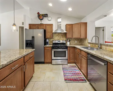 a kitchen with stainless steel appliances granite countertop a stove a sink dishwasher a refrigerator and a oven with wooden floor