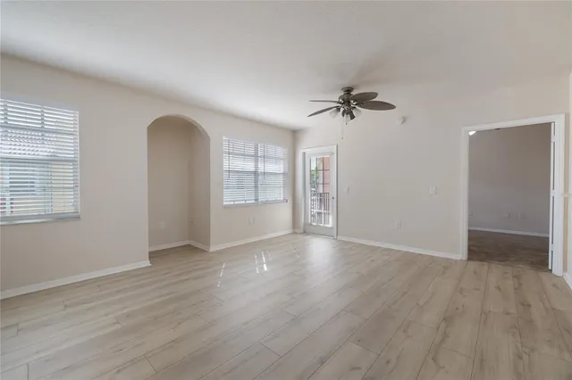 an empty room with wooden floor ceiling fan and windows
