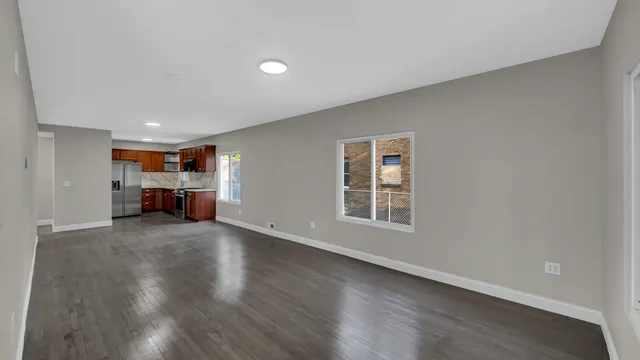 a view of empty room with wooden floor and kitchen