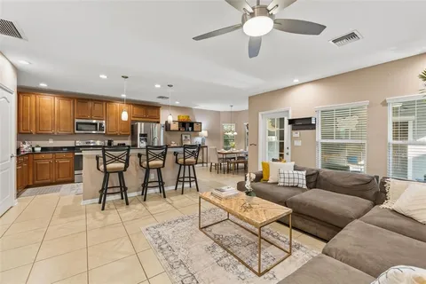 a living room kitchen with stainless steel appliances kitchen island granite countertop a stove a sink a dining table and chairs with wooden floor