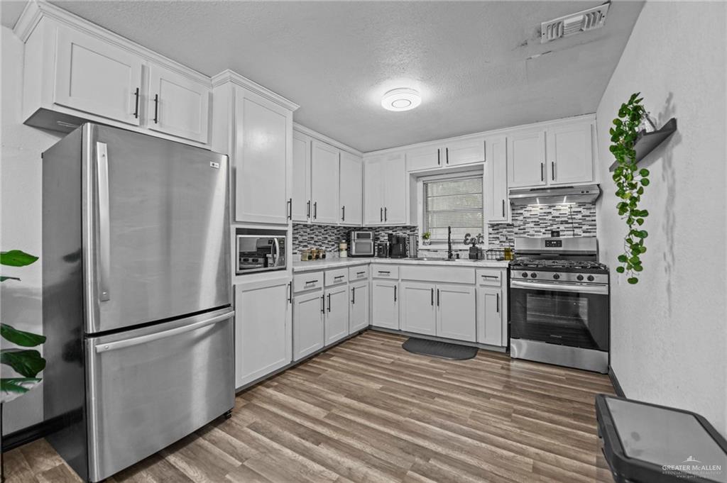 5422 South 28th Street McAllen, TX 78503 - Photo 11 of 21 Kitchen with stainless steel appliances, light countertops, white cabinets, a textured ceiling, and dark wood finished floors