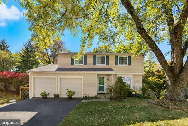 a view of a white house next to a yard with a large tree