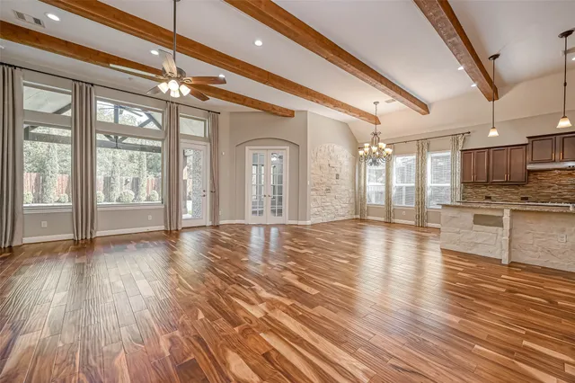 a view of an empty room with wooden floor and a kitchen