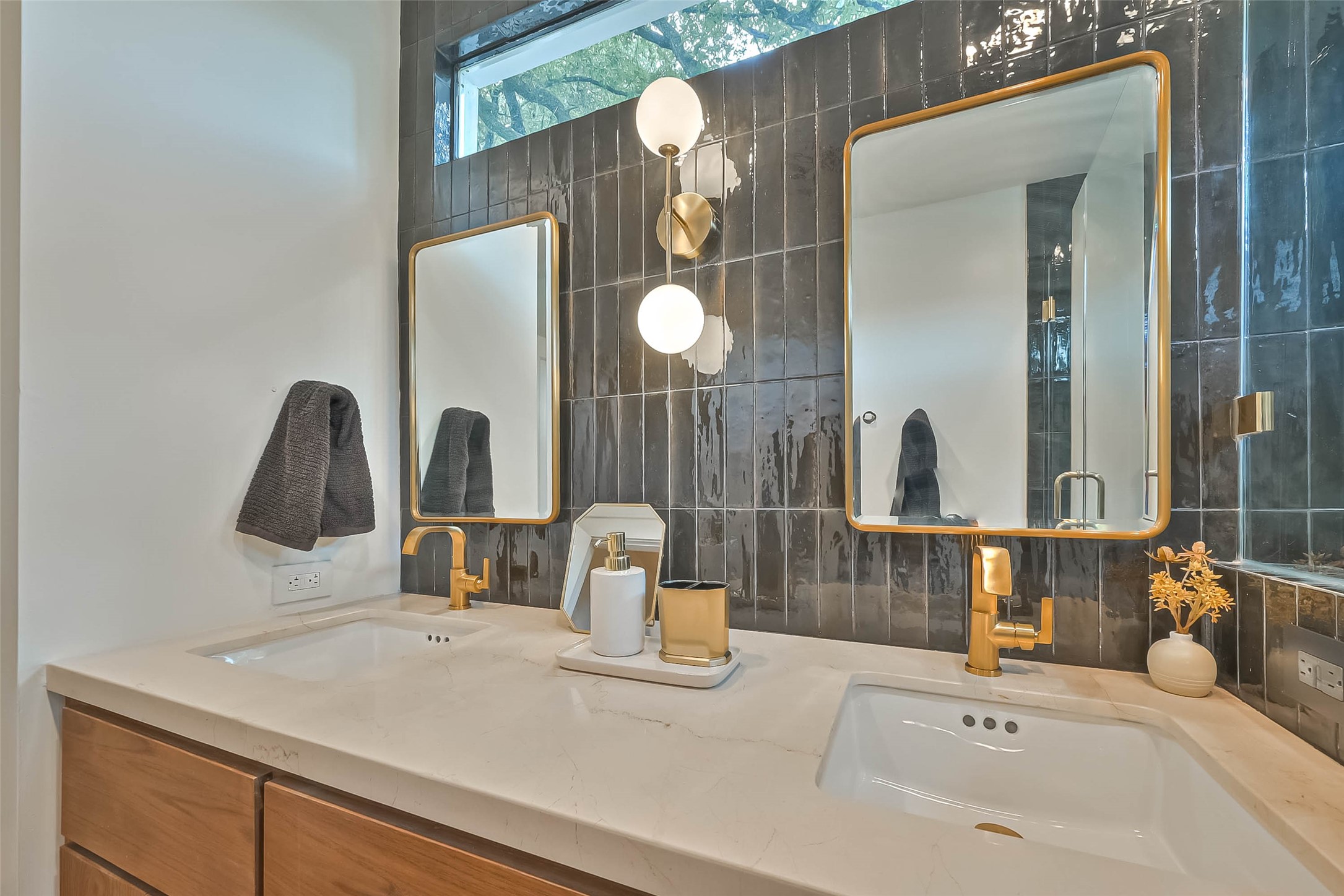 412 Sue Street Houston, TX 77009 - Photo 12 of 19 Another picture of primary bathroom featuring a double vanity with sleek gold fixtures and framed mirrors. The dark, glossy tile wall adds a touch of elegance, complemented by a large window for natural light.