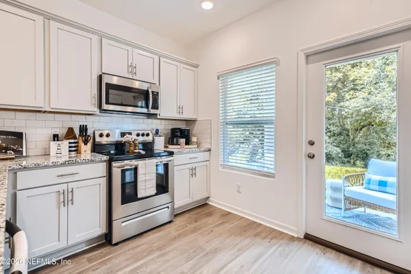 a kitchen with stainless steel appliances granite countertop white cabinets a sink a window and a microwave