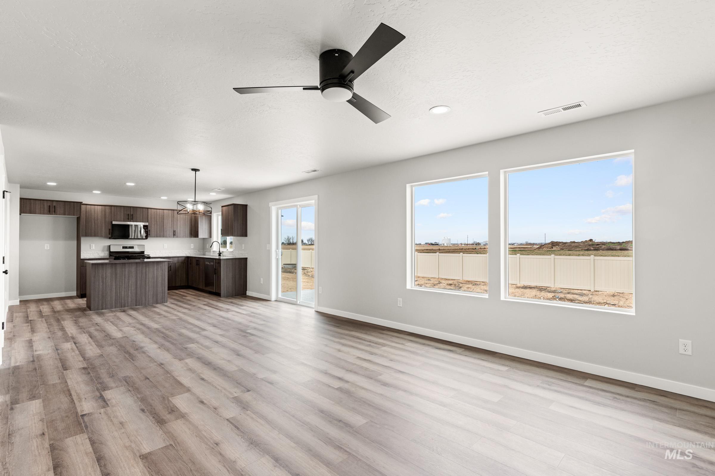 12830 Ropers Street Nampa, ID 83651 - Photo 8 of 18 Open-concept living space featuring wood-finish flooring, a modern kitchen with dark cabinetry, a kitchen island, and a sliding glass door