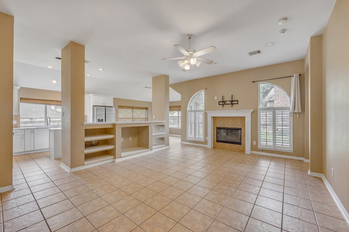 2726 Grimes Ranch Road Austin, TX 78732 - Photo 15 of 35 Unfurnished living room with a ceiling fan, a fireplace, light tile patterned flooring, healthy amount of natural light, and recessed lighting