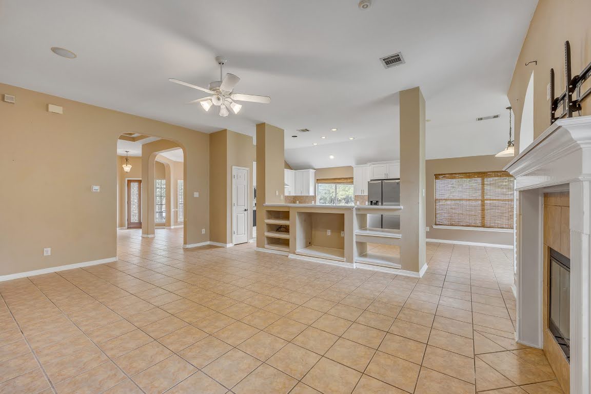 2726 Grimes Ranch Road Austin, TX 78732 - Photo 16 of 35 Unfurnished living room with light tile patterned floors, arched walkways, a fireplace, a ceiling fan, and recessed lighting