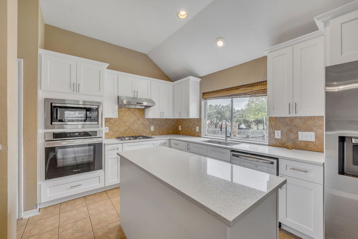 2726 Grimes Ranch Road Austin, TX 78732 - Photo 20 of 35 Kitchen with stainless steel appliances, white cabinets, light stone countertops, light tile patterned floors, and lofted ceiling