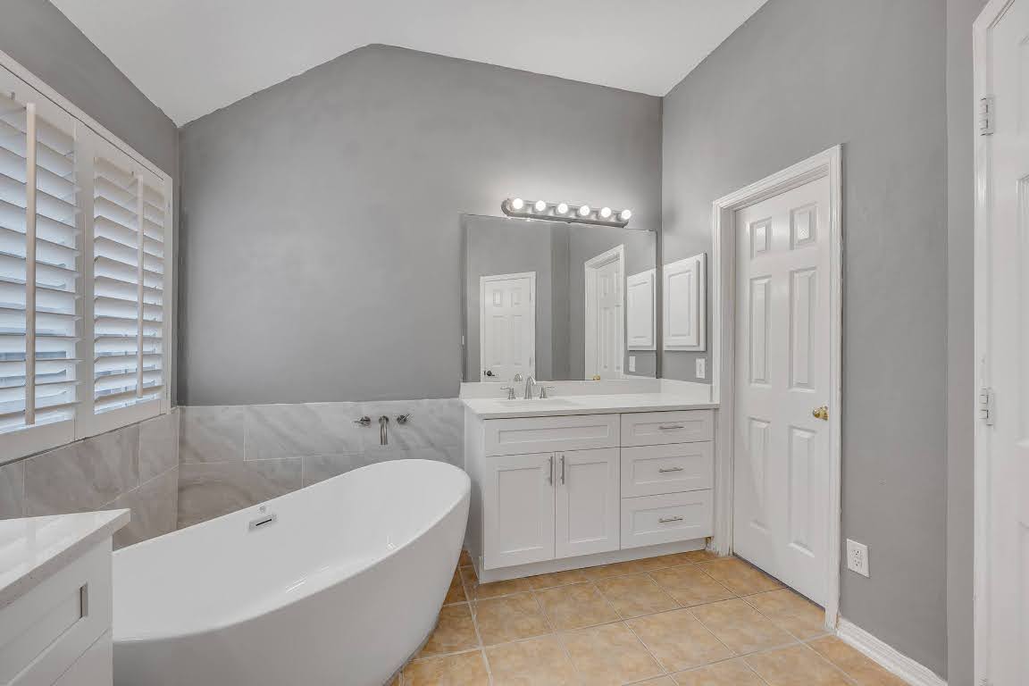 2726 Grimes Ranch Road Austin, TX 78732 - Photo 26 of 35 Full bathroom with vanity, a freestanding bath, light tile patterned flooring, lofted ceiling, and tile walls