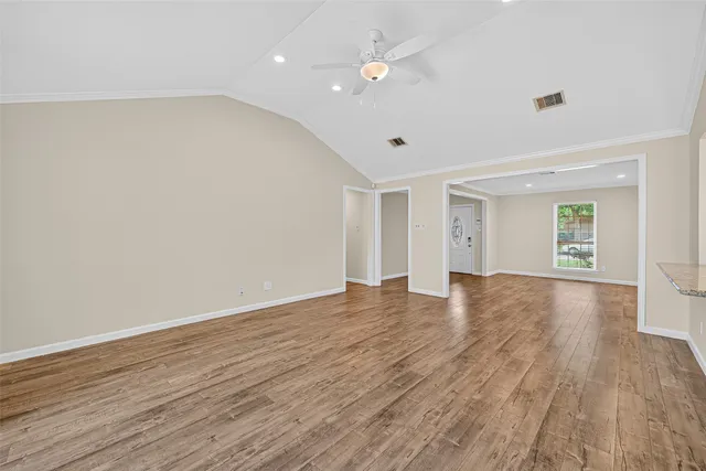 a view of an empty room with wooden floor and a ceiling fan