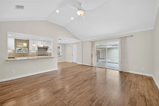 a view of an empty room and kitchen with wooden floor