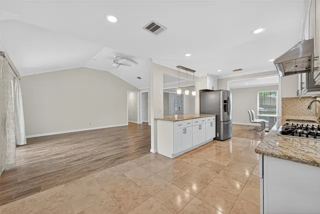 a large white kitchen with stainless steel appliances kitchen island a sink dishwasher a stove and a refrigerator with wooden floor