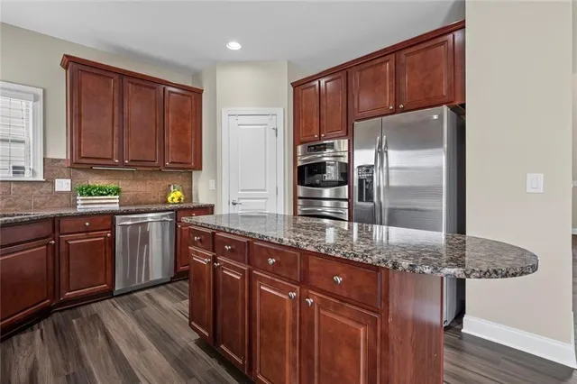 a kitchen with stainless steel appliances granite countertop a refrigerator a sink dishwasher a stove with wooden cabinets and floor