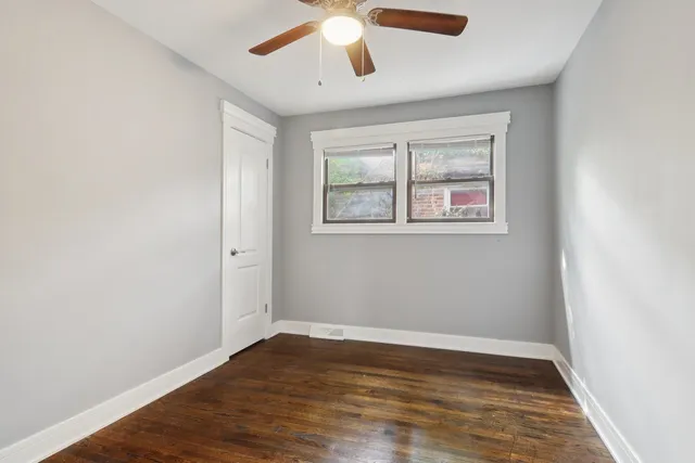 an empty room with wooden floor chandelier fan and windows