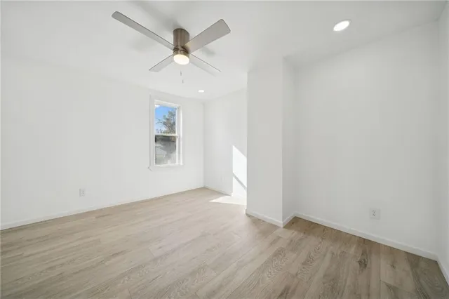 an empty room with wooden floor ceiling fan and windows