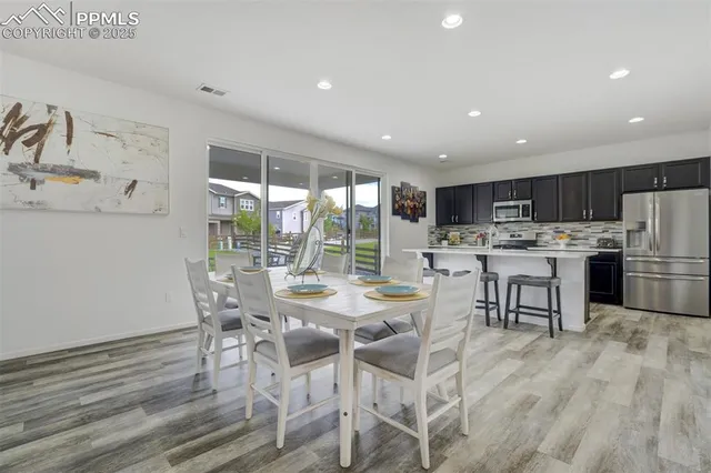 a room with stainless steel appliances kitchen island granite countertop a table chairs and a refrigerator