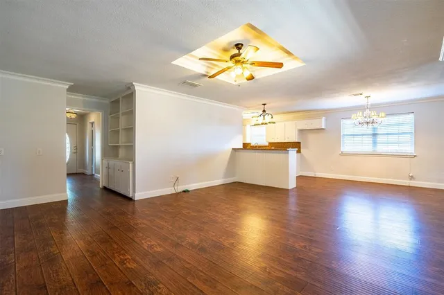 an empty room with wooden floor chandelier and windows