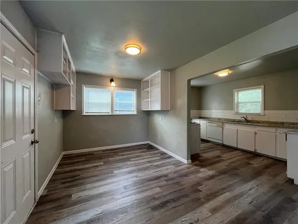 a view of an empty room and kitchen with wooden floor