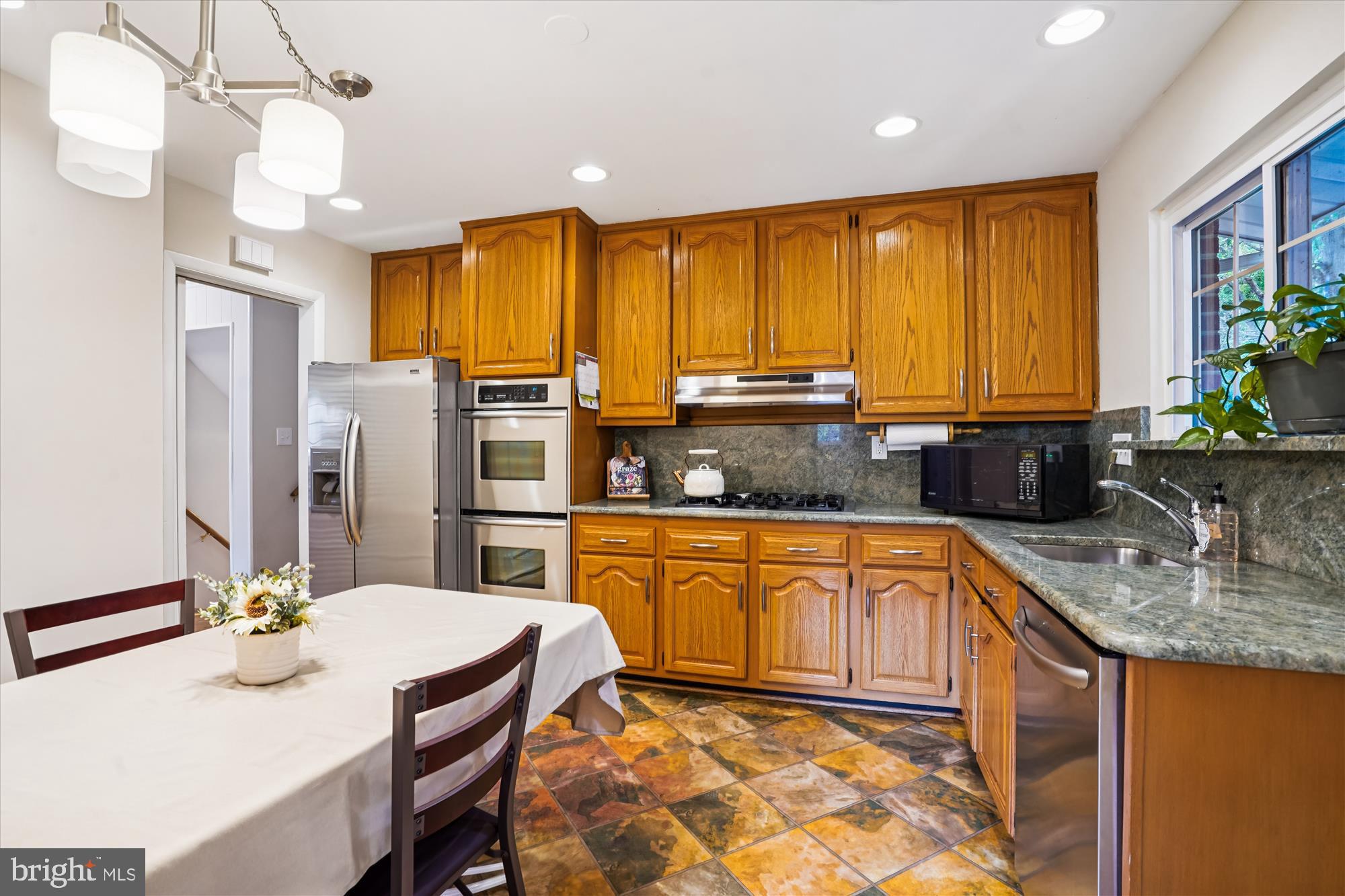 6216 Rockhurst Road Bethesda, MD 20817 - Photo 15 of 52 a kitchen with stainless steel appliances granite countertop a sink a stove a refrigerator a dining table and chairs with wooden floor