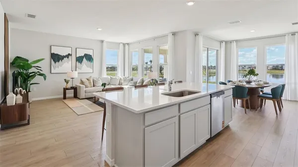 a living room with kitchen island furniture a potted plant and a large window