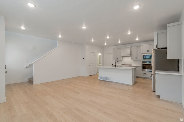 30 South Moonlit Road Mapleton, UT 84664 - Photo 6 of 25 Open-concept living space featuring wood-finish flooring, a modern kitchen island with an integrated sink and matte black faucet, light gray cabinetry, stainless steel appliances, and recessed lighting throughout
