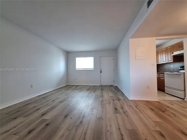 a view of an empty room with wooden floor and a window