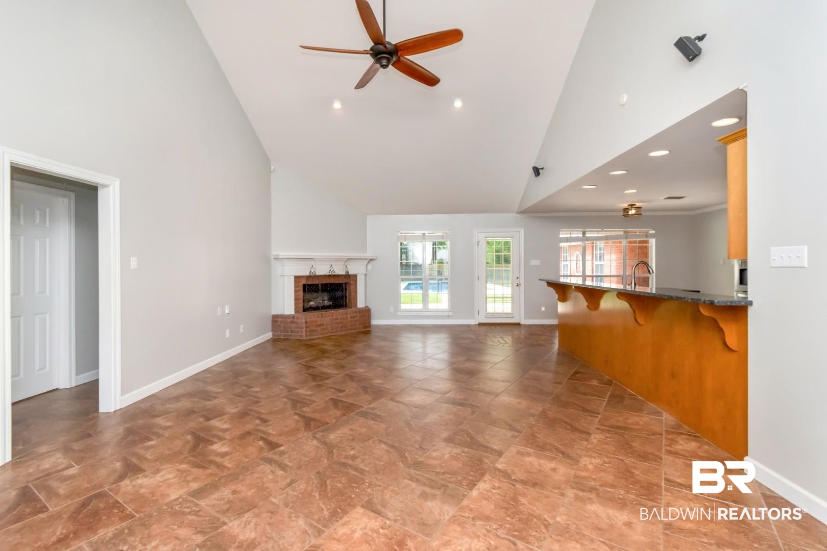 10691 Hunters Ridge Drive Mobile, AL 36695 - Photo 6 of 37 Vaulted ceiling living area featuring a brick fireplace with a white mantel, tiled flooring, ceiling fan, and an integrated breakfast bar with a granite-style countertop