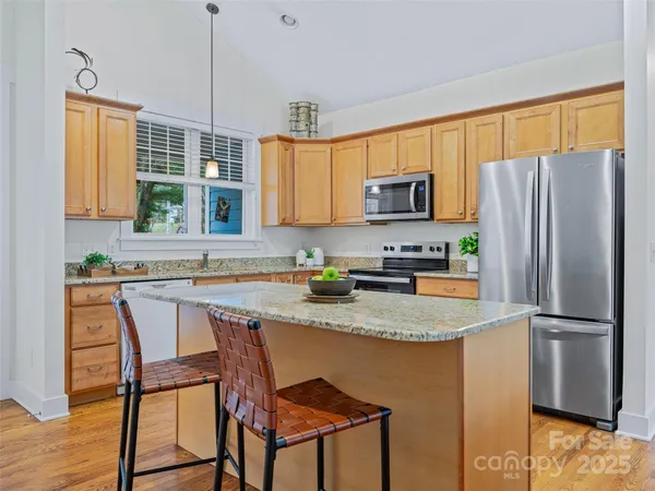 a kitchen with stainless steel appliances granite countertop a refrigerator a stove a sink a dining table and chairs with wooden floor