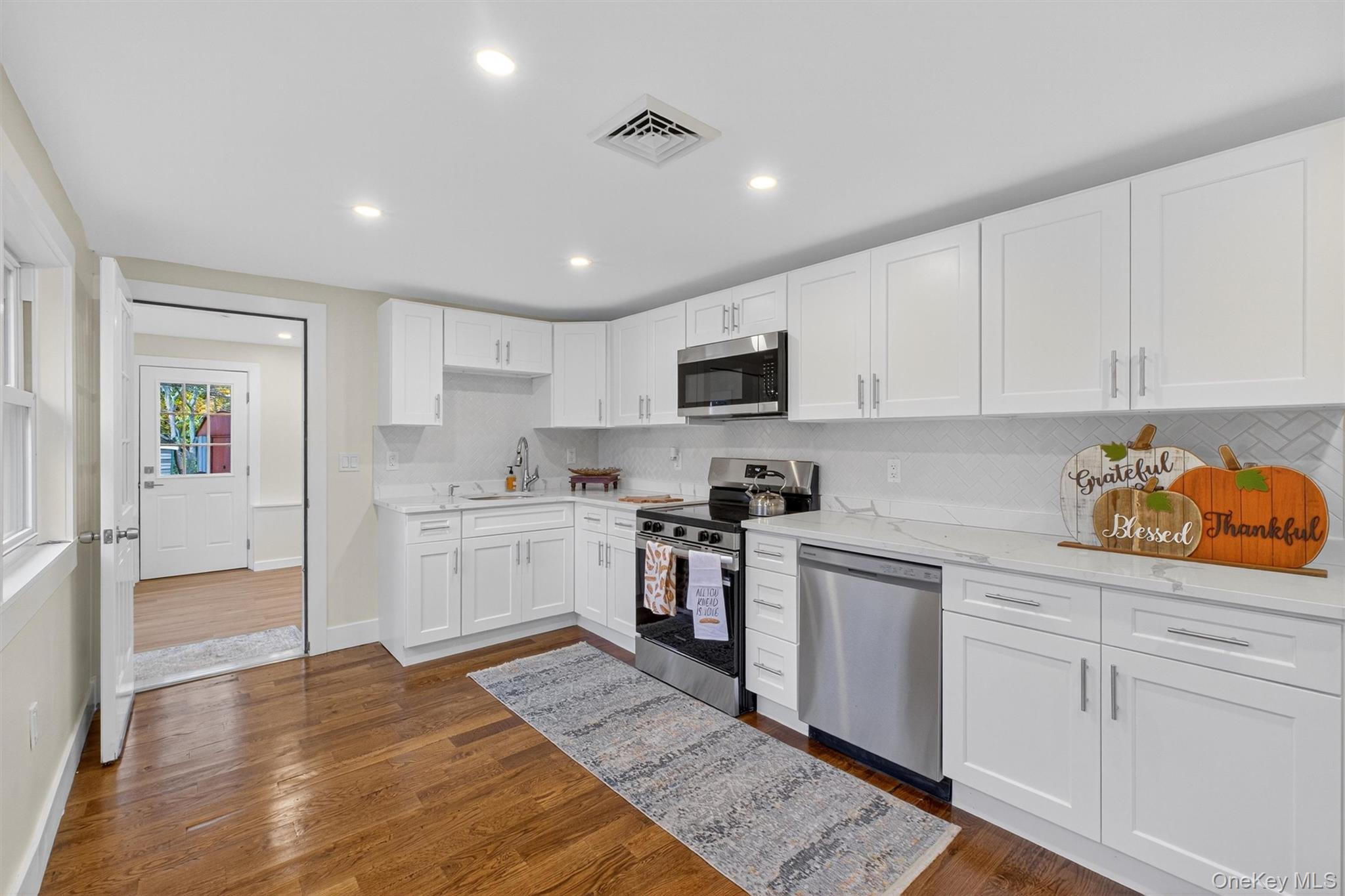 86 Vassar Road Poughkeepsie, NY 12603 - Photo 10 of 31 Kitchen with stainless steel appliances, white cabinetry, dark wood finished floors, tasteful backsplash, and light stone counters