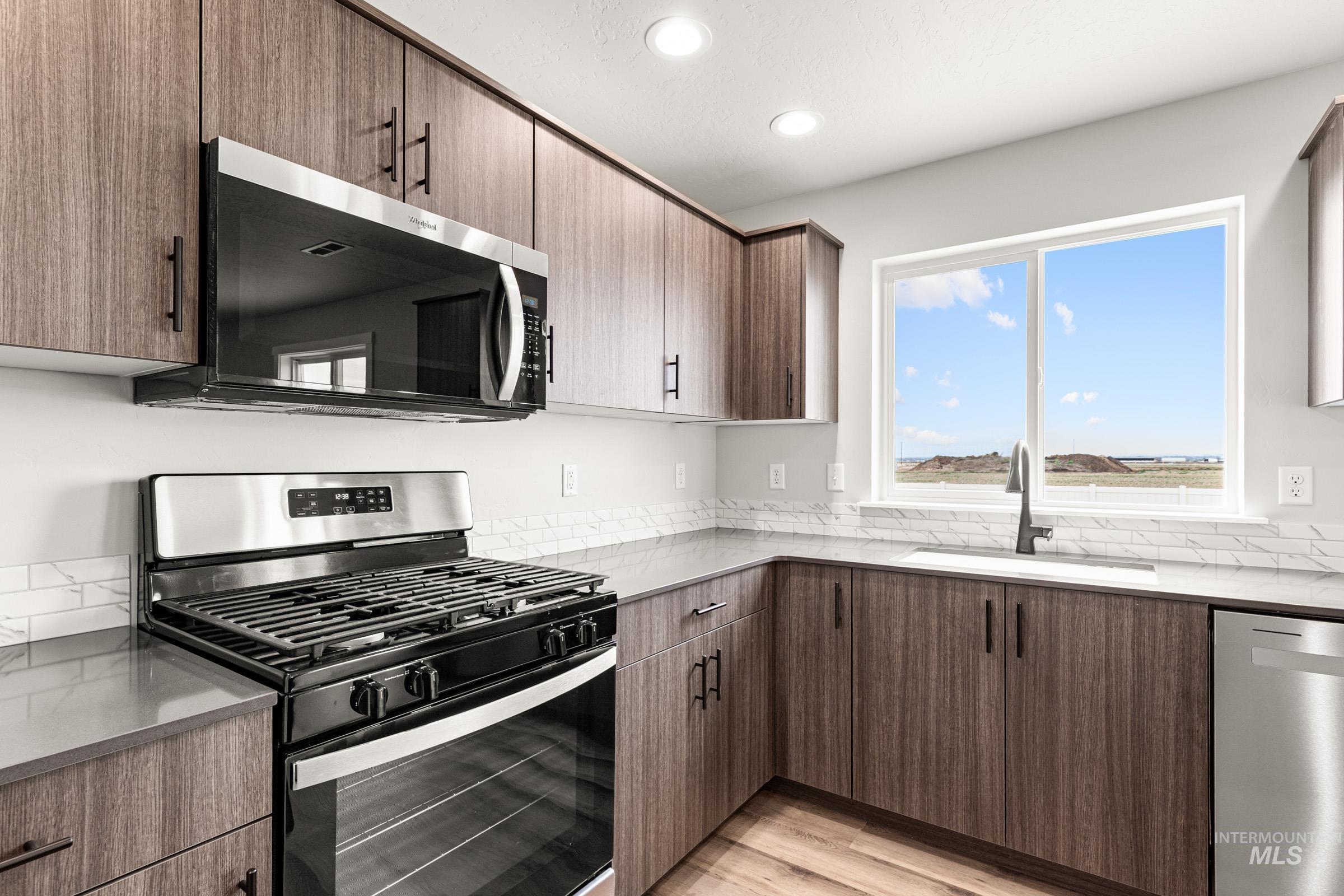 12830 Ropers Street Nampa, ID 83651 - Photo 5 of 18 Kitchen featuring wood-finish cabinetry, stainless steel appliances, light countertops, a subway tile backsplash, and wood-finish flooring