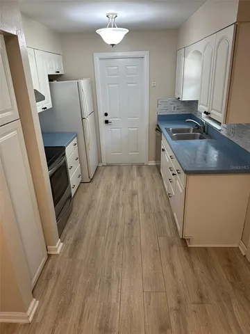 a kitchen with granite countertop a refrigerator a sink dishwasher a stove and white countertops with wooden floor