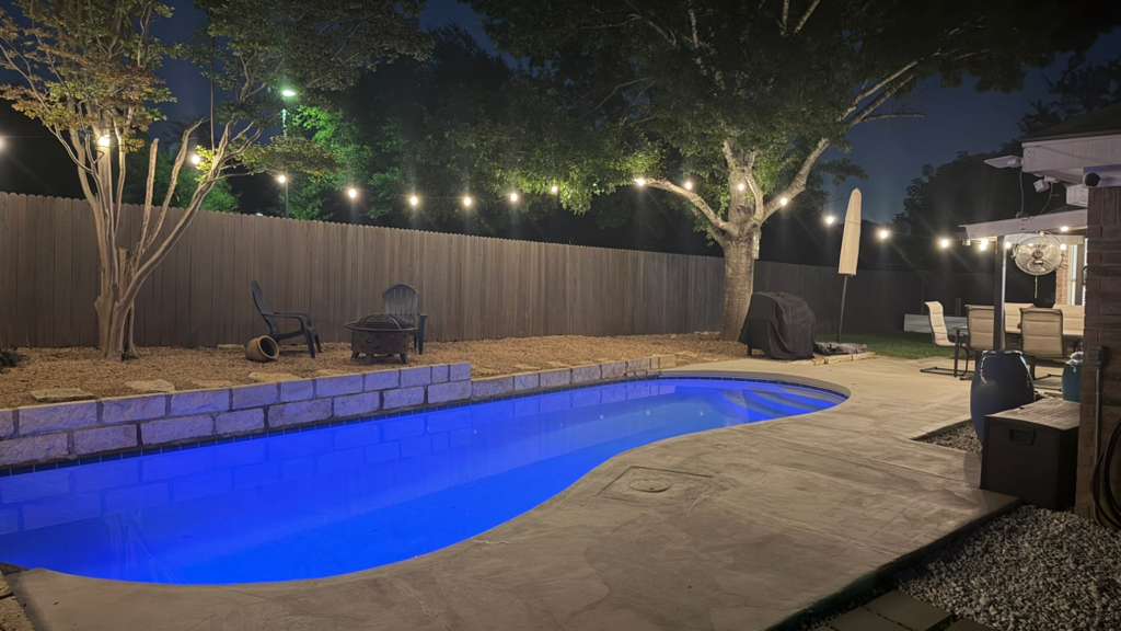 9024 Heiden Lane Austin, TX 78749 - Photo 23 of 28 Backyard with a blue-lit inground pool, concrete decking, and a stone-faced retaining wall