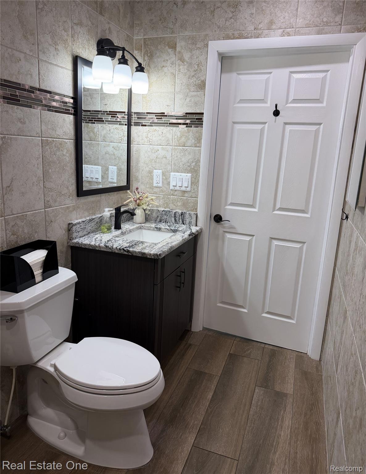 1115 Torpey Road Troy, MI 48083 - Photo 31 of 38 Bathroom featuring large format wall tile with a decorative mosaic accent, dark wood-finish vanity with a stone countertop, a rectangular mirror, and a three-light fixture
