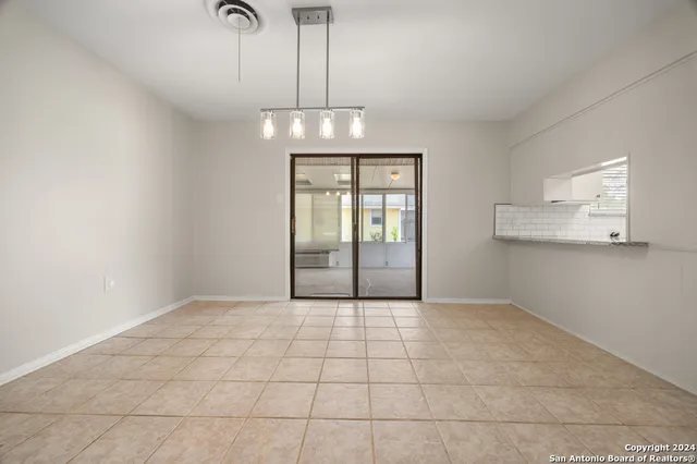 a view of an empty room with chandelier and kitchen view
