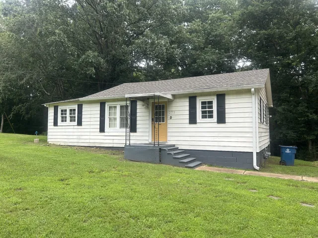 a white house that has a small yard and large trees