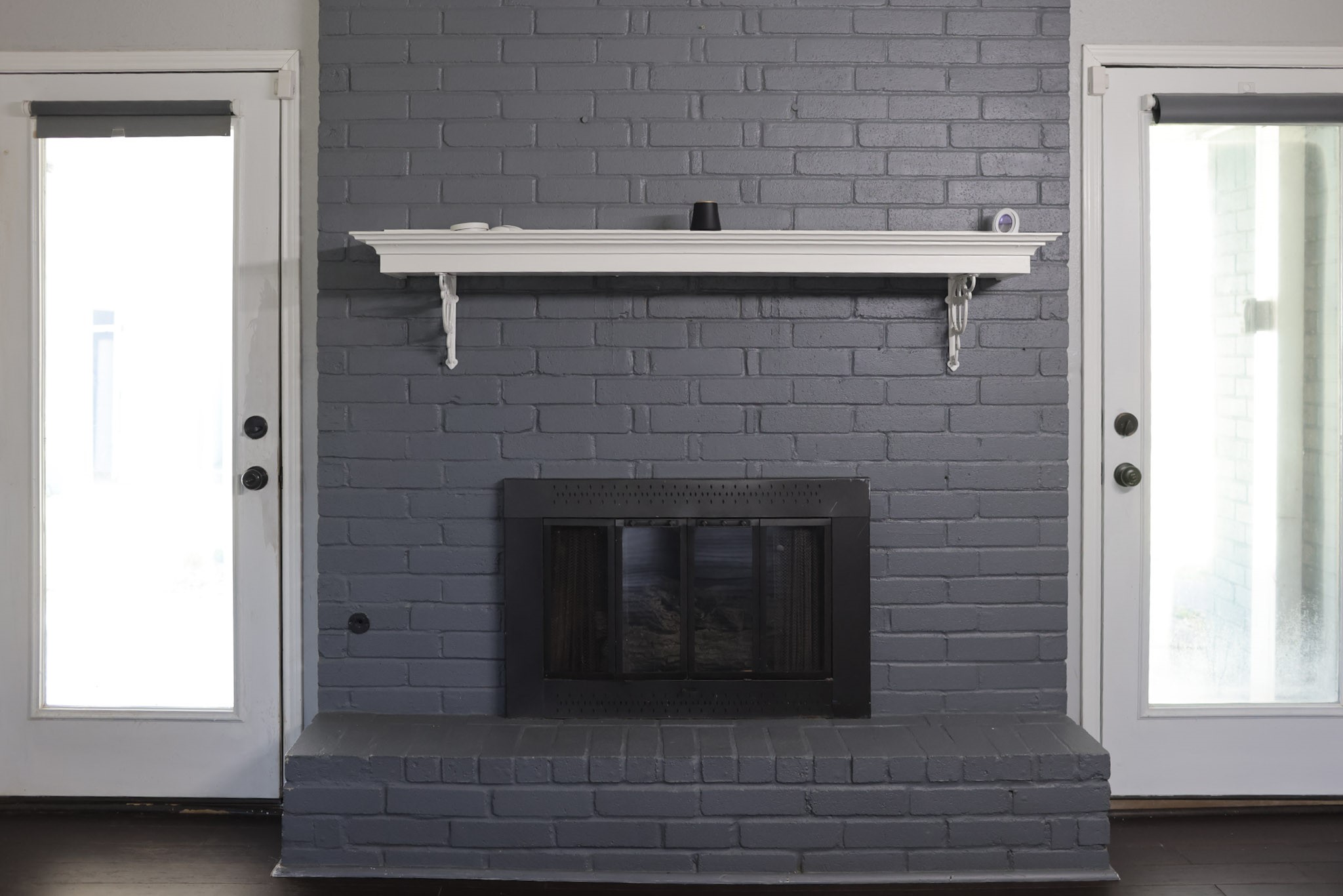 407 Tamarind Street Lake Jackson, TX 77566 - Photo 21 of 36 This photo features a stylish gray brick fireplace with a white mantel, flanked by two glass doors, offering a sleek and modern look for any living space.