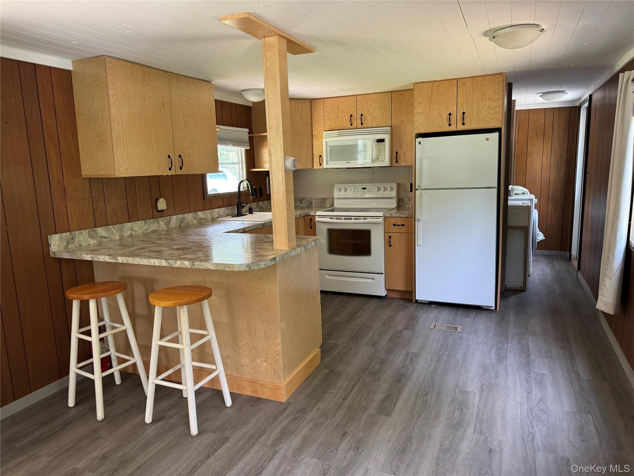 204 Mongaup Road Fallsburg, NY 12747 - Photo 2 of 10 Kitchen with wooden walls, white appliances, a kitchen breakfast bar, dark wood finished floors, and light countertops