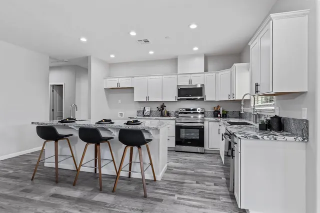a kitchen with stainless steel appliances kitchen island granite countertop a stove top oven a sink dishwasher and white cabinets with wooden floor