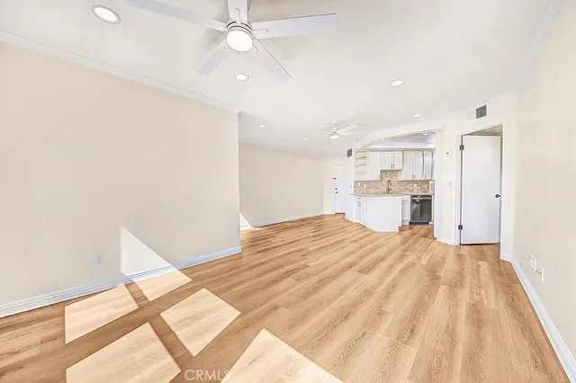 a big room with wooden floor a ceiling fan and kitchen view