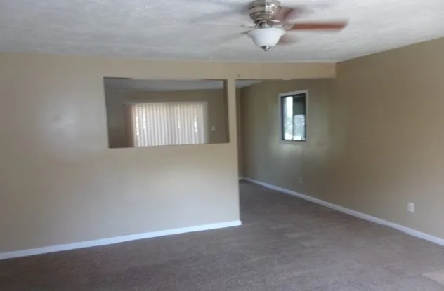 an empty room with a chandelier fan and windows