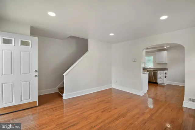an empty room with wooden floor and a kitchen