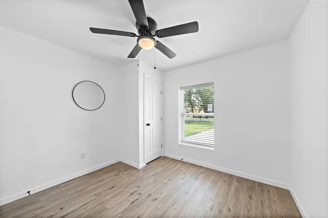 an empty room with wooden floor fan and windows