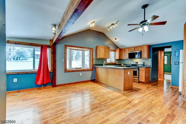a kitchen with stainless steel appliances kitchen island granite countertop a refrigerator a sink dishwasher a dining table and chairs with wooden floor